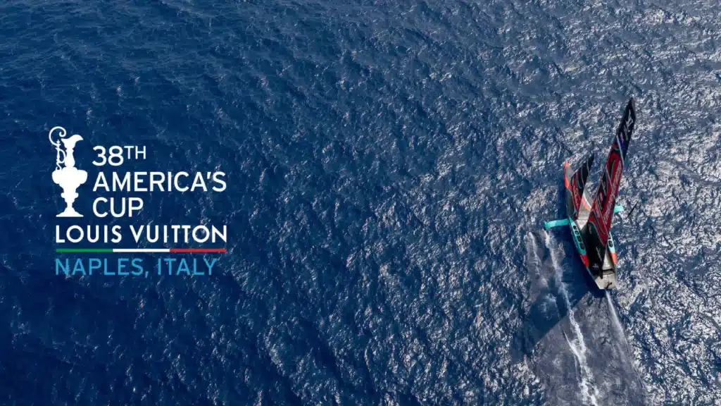 Logo ufficiale della 38ª America’s Cup Louis Vuitton con vista aerea di un’imbarcazione nel Golfo di Napoli.
