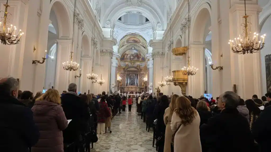 Interno della Chiesa Cattedrale di Aversa durante una celebrazione, con fedeli raccolti nella navata centrale sotto le volte storiche.